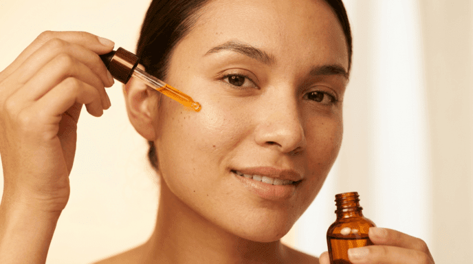 Woman holding an amber vitamin C serum dropper