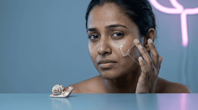 Woman raising one eyebrow while applying stringy snail mucin gel